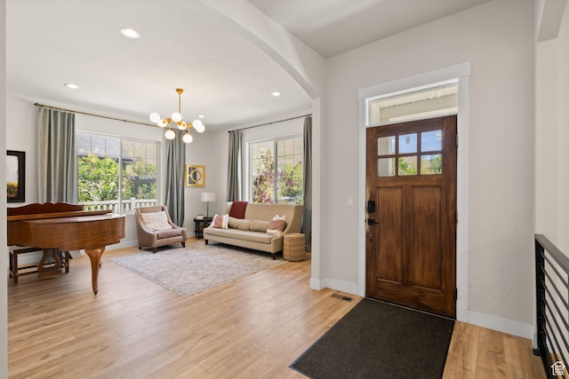 foyer featuring arched walkways, light wood-style flooring, a chandelier, recessed lighting, and baseboards