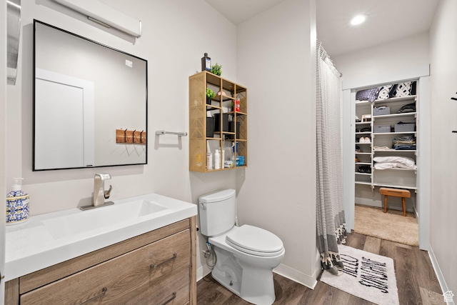 bathroom featuring toilet, wood finished floors, vanity, baseboards, and recessed lighting