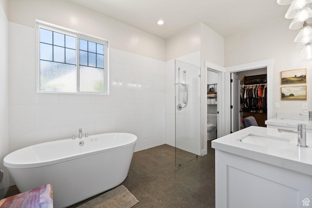 bathroom featuring walk in shower, a freestanding tub, vanity, and a walk in closet
