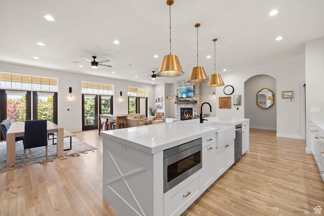 kitchen featuring stainless steel appliances, a sink, recessed lighting, a large fireplace, and light wood finished floors