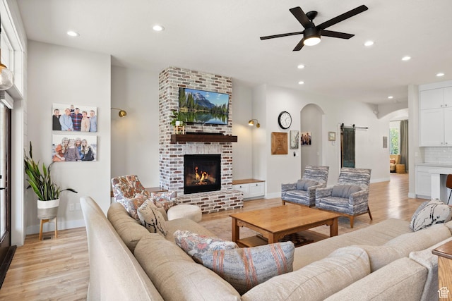 living room featuring arched walkways, a brick fireplace, recessed lighting, light wood-style floors, and a ceiling fan