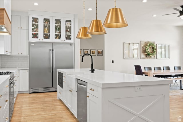 kitchen featuring built in appliances, light wood-type flooring, a kitchen island with sink, recessed lighting, and white cabinets