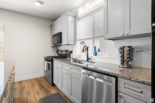 kitchen featuring stainless steel appliances, a sink, decorative backsplash, dark stone counters, and baseboards