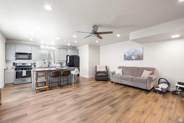 living room featuring baseboards, recessed lighting, light wood-type flooring, and a ceiling fan