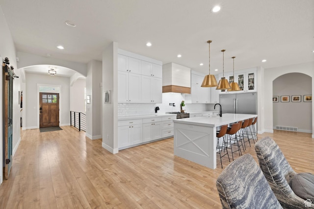 kitchen featuring decorative backsplash, light countertops, arched walkways, light wood finished floors, and a kitchen bar