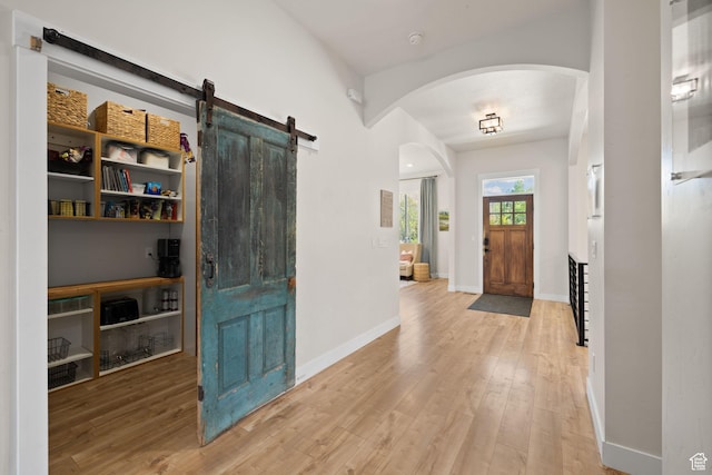 foyer entrance featuring arched walkways, a barn door, wood finished floors, and baseboards