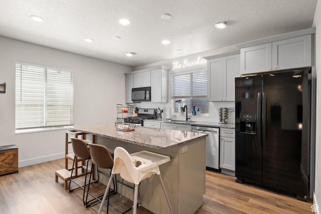 kitchen featuring black appliances, a sink, a kitchen island, a kitchen bar, and tasteful backsplash