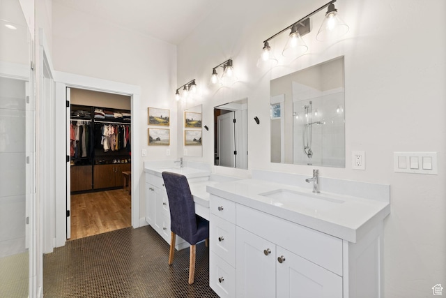 bathroom featuring a tile shower, two vanities, and a walk in closet