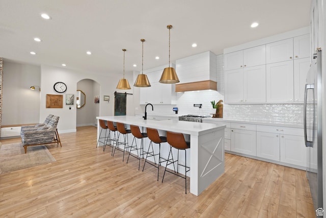 kitchen featuring arched walkways, custom range hood, recessed lighting, stainless steel fridge, and light countertops