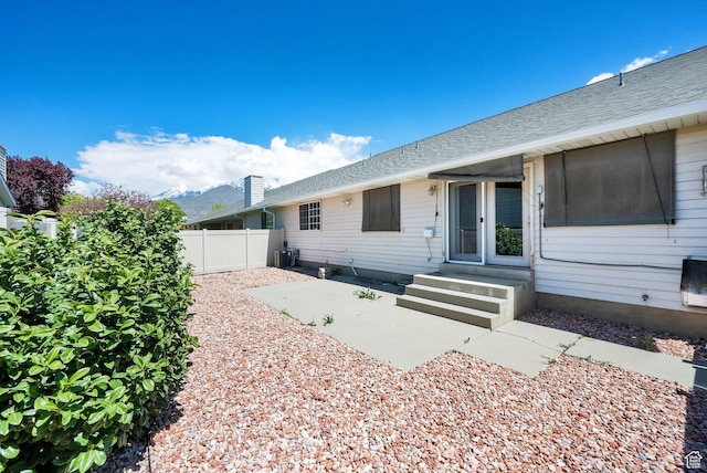 doorway to property with fence, roof with shingles, and a patio