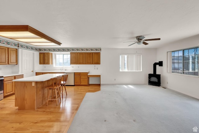 kitchen with stainless steel dishwasher, a kitchen bar, a ceiling fan, light countertops, and a wood stove