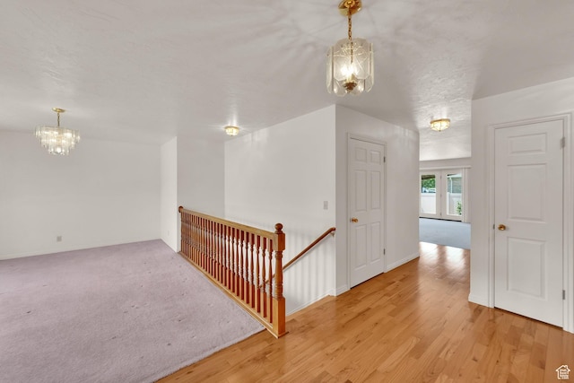 hallway featuring a chandelier, an upstairs landing, wood finished floors, and baseboards