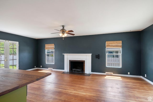 unfurnished living room featuring ceiling fan, a fireplace with flush hearth, wood finished floors, baseboards, and french doors