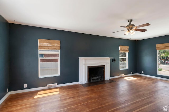 unfurnished living room with a ceiling fan, a fireplace with flush hearth, wood finished floors, and baseboards