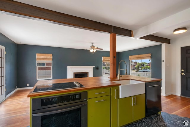 kitchen with wood counters, black appliances, a sink, green cabinets, and light wood-type flooring