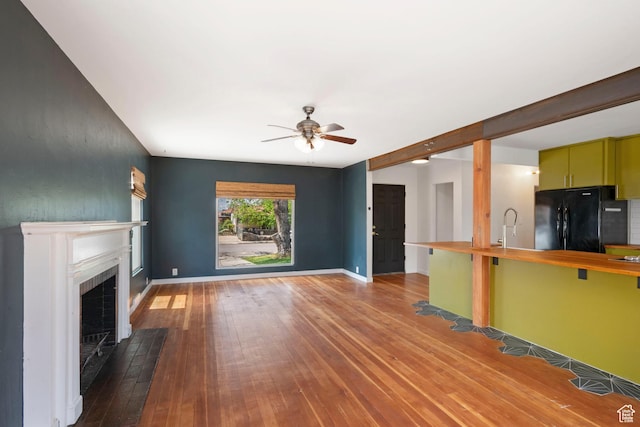 unfurnished living room featuring ceiling fan, a fireplace with flush hearth, wood-type flooring, and baseboards