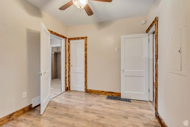 unfurnished bedroom featuring light wood-style flooring, electric panel, baseboards, and ceiling fan