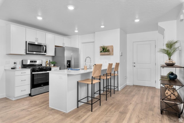 kitchen with stainless steel appliances, light wood-style flooring, a breakfast bar area, light countertops, and white cabinetry