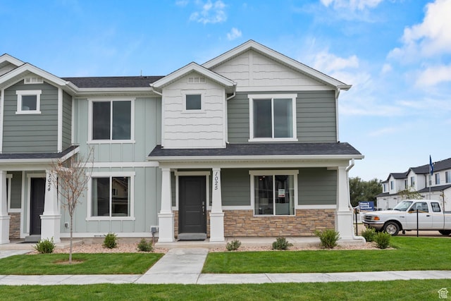 craftsman house with stone siding, board and batten siding, a front yard, and a porch