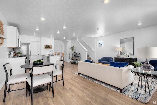 living area featuring stairway, recessed lighting, light wood-style flooring, and a textured ceiling
