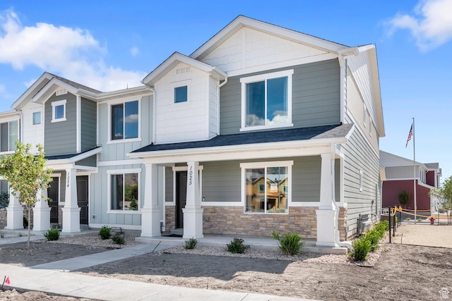 craftsman-style house with covered porch, stone siding, and roof with shingles