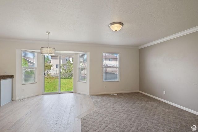 spare room featuring crown molding, healthy amount of natural light, a textured ceiling, wood finished floors, and baseboards