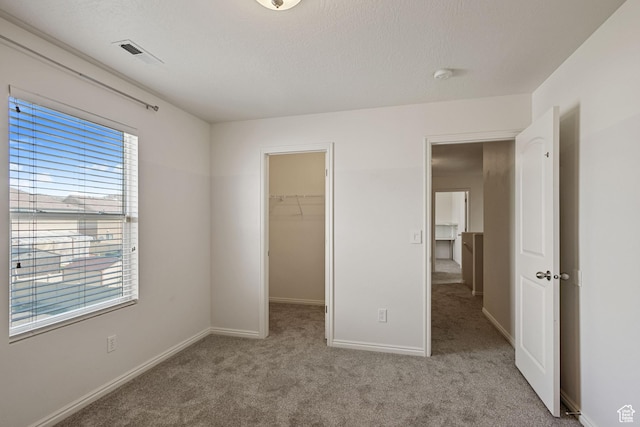 unfurnished bedroom with carpet, a spacious closet, baseboards, and a closet