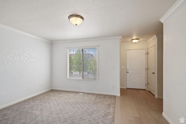 spare room featuring ornamental molding, light wood-style flooring, a textured ceiling, and baseboards