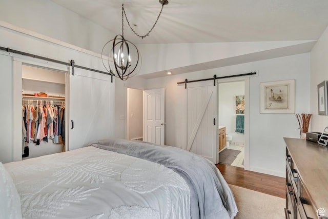 bedroom with a barn door, lofted ceiling, wood finished floors, a spacious closet, and baseboards