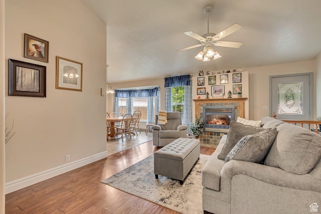 living area with baseboards, wood finished floors, a ceiling fan, a tiled fireplace, and lofted ceiling
