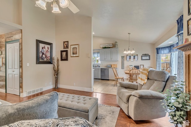 living area featuring vaulted ceiling, plenty of natural light, a chandelier, ceiling fan, and light wood finished floors