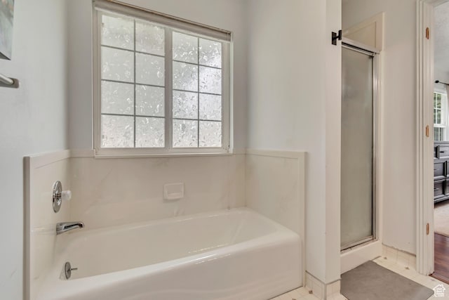 bathroom with healthy amount of natural light, a stall shower, a bath, and baseboards