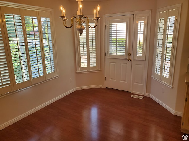 unfurnished dining area with a chandelier, dark wood finished floors, baseboards, and healthy amount of natural light