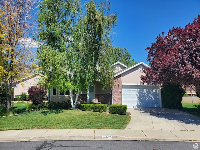 view of property hidden behind natural elements with an attached garage, concrete driveway, a front lawn, brick siding, and stucco siding