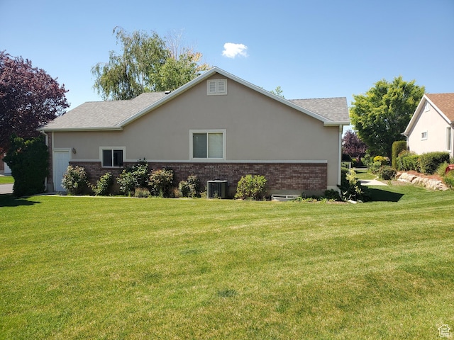 view of home's exterior with a lawn, brick siding, stucco siding, central air condition unit, and a shingled roof