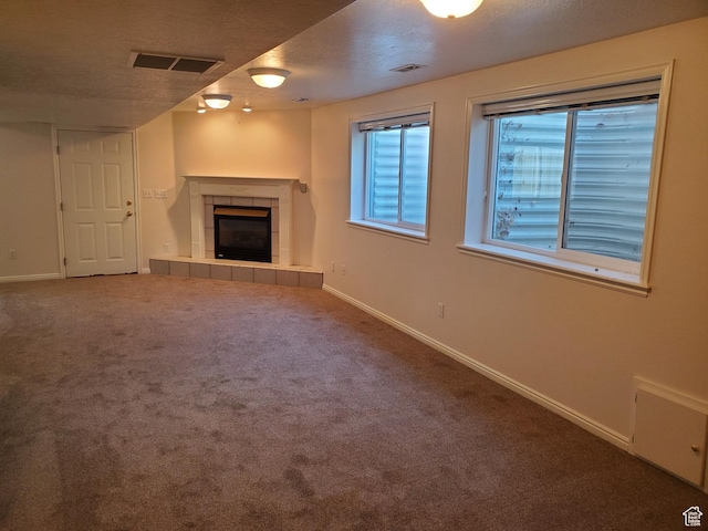 unfurnished living room with a tile fireplace, carpet flooring, baseboards, and a textured ceiling