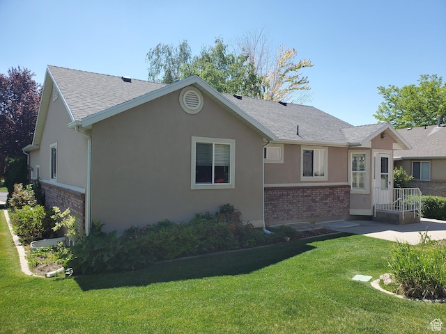 view of front facade featuring brick siding, roof with shingles, stucco siding, a front lawn, and a patio