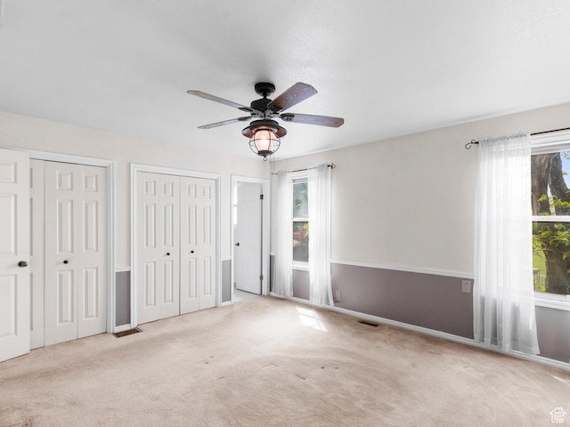 unfurnished bedroom with two closets, carpet floors, baseboards, and a ceiling fan