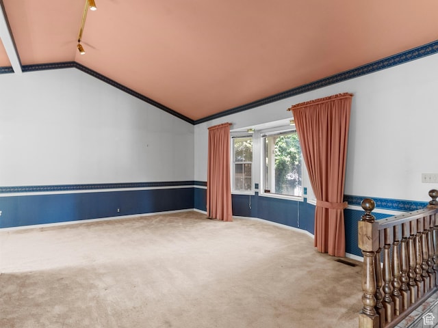 carpeted empty room with lofted ceiling, baseboards, ornamental molding, and track lighting