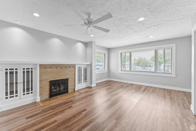 unfurnished living room with wood finished floors, a textured ceiling, a fireplace, baseboards, and a ceiling fan