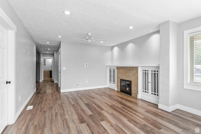 unfurnished living room featuring attic access, a ceiling fan, wood finished floors, a textured ceiling, and a fireplace with flush hearth