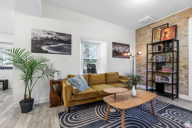 living area with wood finished floors, baseboards, a textured ceiling, and brick wall