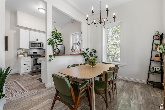 dining area featuring a chandelier, light wood-style flooring, and baseboards