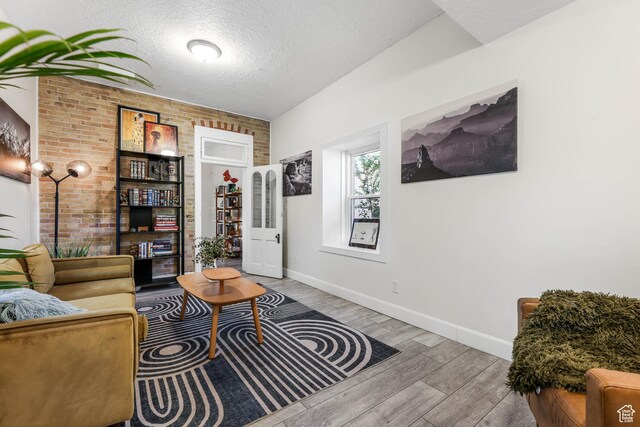 living room featuring wood finished floors, baseboards, brick wall, and a textured ceiling