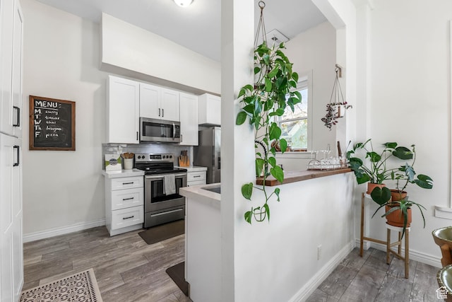 kitchen featuring stainless steel appliances, wood finished floors, light countertops, and white cabinets