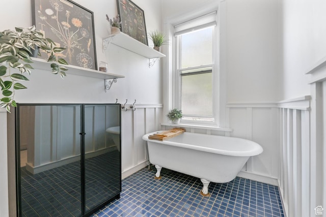 full bathroom featuring a wainscoted wall, a decorative wall, a soaking tub, and tile patterned flooring