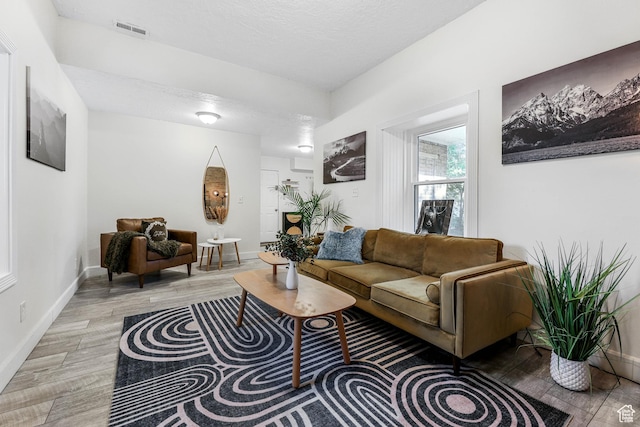 living room featuring baseboards, light wood-style floors, and a textured ceiling