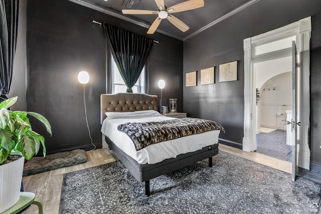bedroom with arched walkways, ornamental molding, wood finished floors, and a ceiling fan
