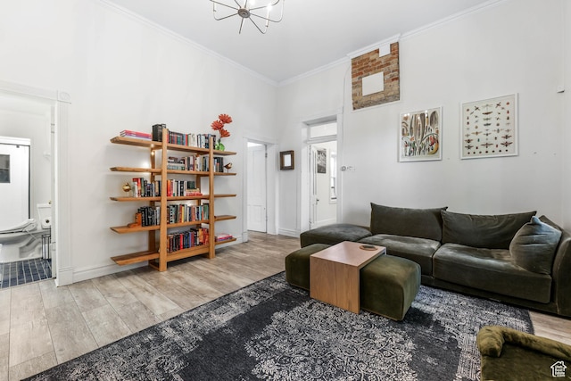 living area with a chandelier, wood finished floors, ornamental molding, a high ceiling, and baseboards