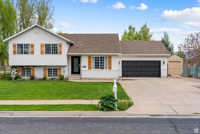 split level home featuring an attached garage, a front lawn, concrete driveway, roof with shingles, and a storage shed